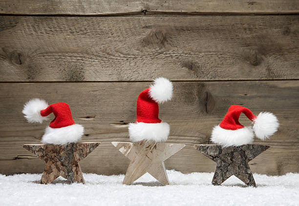 Three wooden stars with santa hats on wooden background - handmade idea for a greeting card