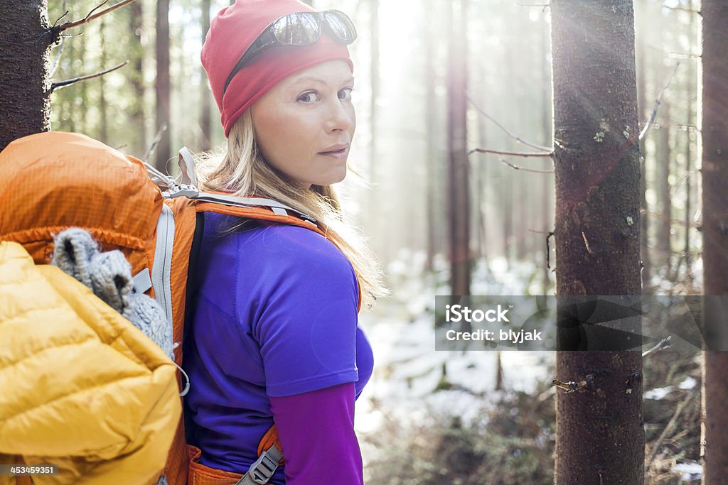 Woman hiking in winter forest sunlight Woman hiking in white winter forest, backlight by morning sunlight rays, recreation and healthy lifestyle outdoors in nature. Beauty blond hiker backpacker looking at camera on sunset. Active Lifestyle Stock Photo