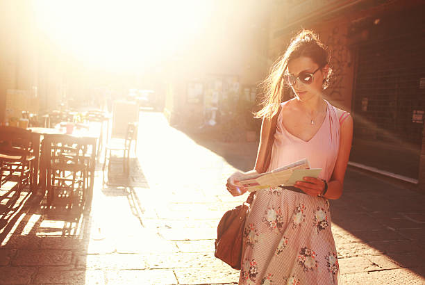 street style fashion young brunette sightseeing on the street, looking at the map, lit by the magic hour sunlight. preppy fashion stock pictures, royalty-free photos & images