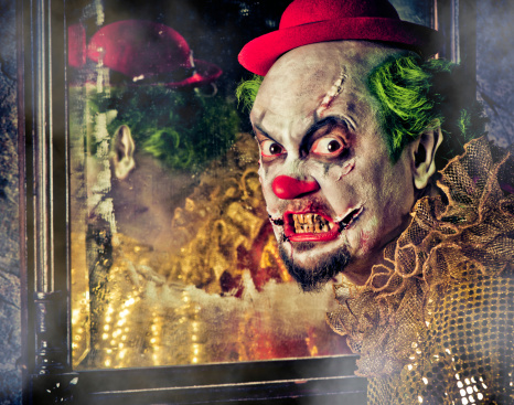 Close up photo of a scary clown mask costume for halloween.The mask has a red bright curly hair. The eys is black and has blue shadow. it has a big red lips. The face is white.