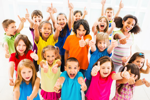 Large group of cheerful children showing thumbs up and looking at the camera.  