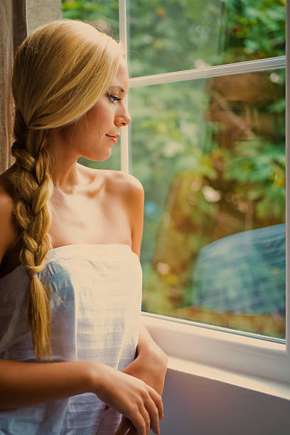 Beautiful young woman looking thrue window with reflection at glass