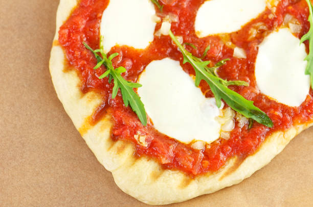 Grilled pizza with tomato sauce, garlic, onions, mozzarella cheese and rustic arugula on parchment paper from above