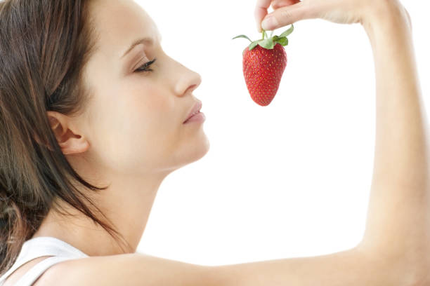 istock Side view of a young female holding a strawberry on white 453472377