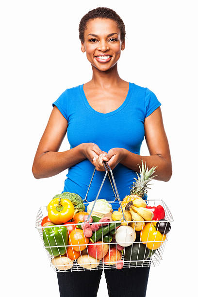 African American Woman Holding  Basket Of Fresh Groceries - Isolated Portrait of a smiling African American woman holding a basket of fresh fruits and vegetables. Vertical shot. Isolated on white. holding shopping basket stock pictures, royalty-free photos & images