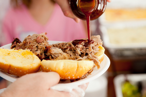 Adding barbeque sauce to a pulled pork sandwich.