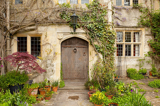 This is Abbey House in Malmesbury, England.  The house was built in the 16th century.  The house's main entrance through an old wooden door, shown here, is surrounded by potted plants and flanked by a small medieval stone statue.
