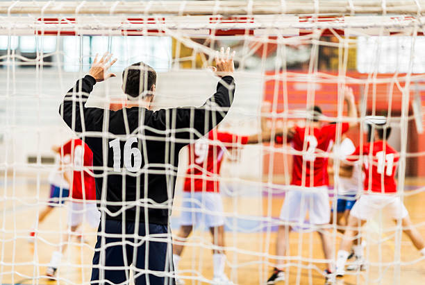 Handball match. View of handball match from the goalkeeper's net. Focus is on goalkeeper with raised hands.    team handball stock pictures, royalty-free photos & images