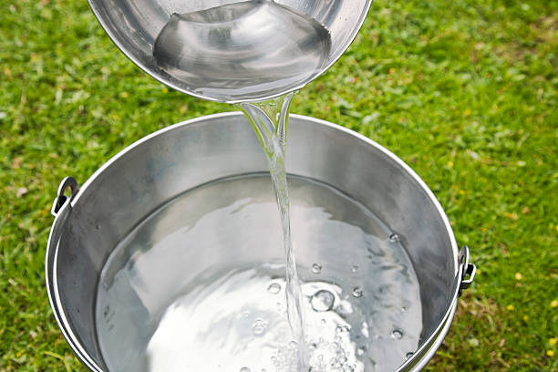 Pouring fresh water from ladle into a bucket. stock photo
