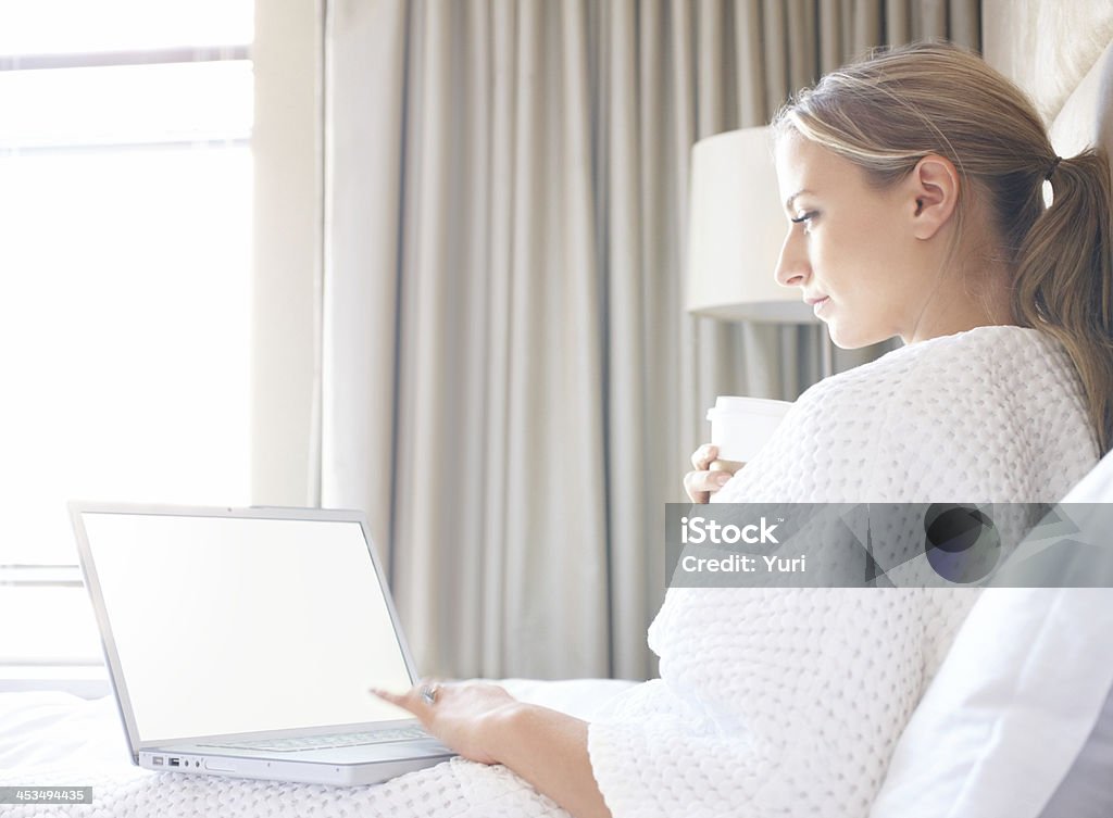 Felice donna seduta sul letto, utilizzando un computer portatile - Foto stock royalty-free di Adulto