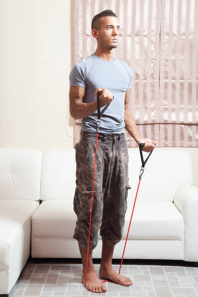istock Slim Muscular male using resistance bands at home. bicep curls 453497239