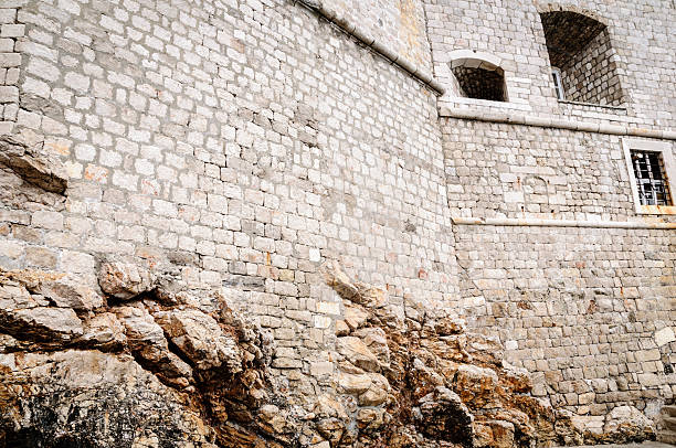 Fortress walls built above the coastal rocks.  The walls appear to blend into the natural rock. Dubrovnik, Croatia.