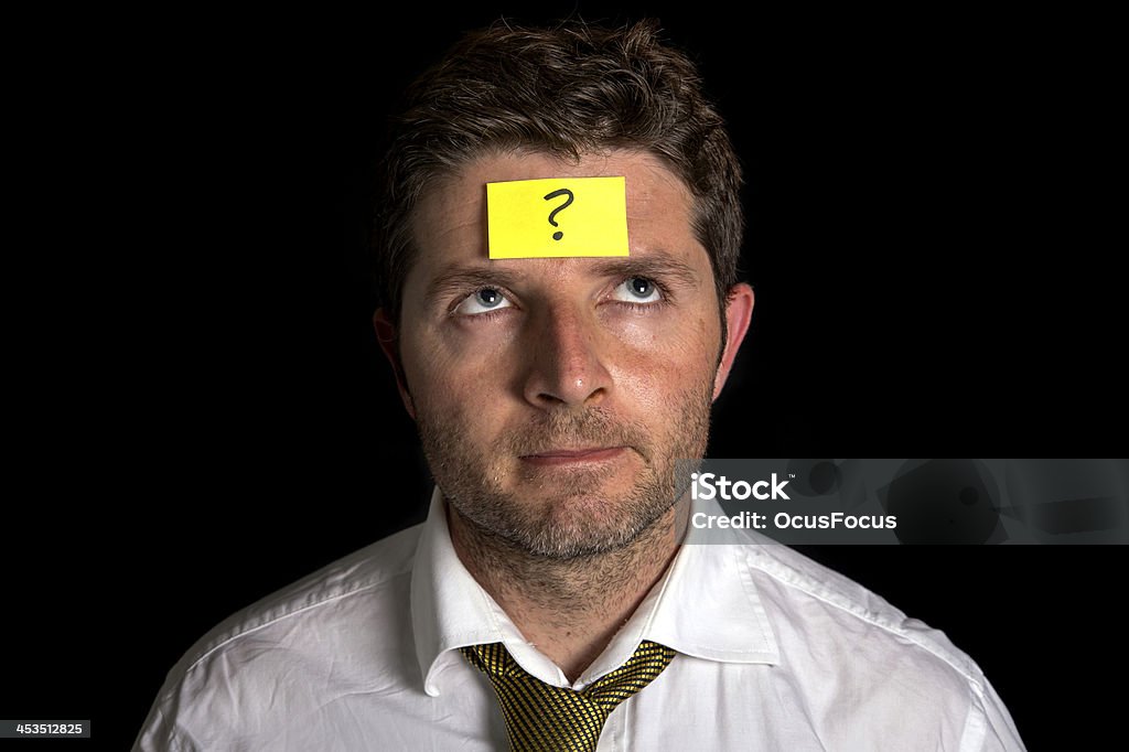 Man with Yellow Postit Note on his Forehead Business man on a black background with a yellow posit note on his face with a question mark written on it. Adhesive Note Stock Photo