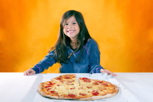 Cute little girl with long hair has blue sweater cheerful expression in front of a pizza
