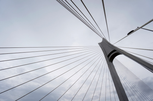 Suspension bridge abstract, against cloudy sky.