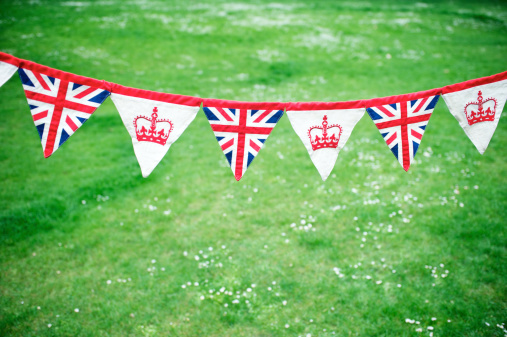 Union Jack and royal crown decorative bunting stands out against bright green spring grass background celebrating the Royal Baby