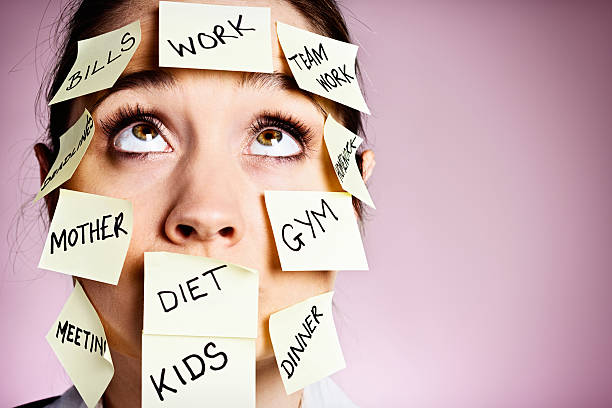 An overworked and overtired woman covered with Post-it reminders for all sorts of tasks and reminders from mother to meeting rolls her eyes in frustration. She's seriously over committed.