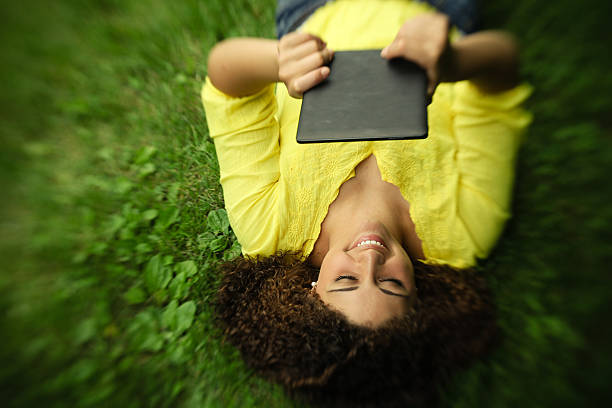 Beautiful teen girl smiling with tablet outside on grass stock photo