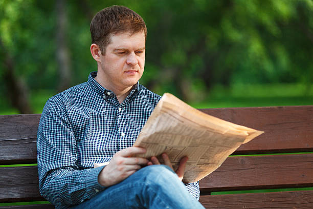 istock Man reads newspaper on bench in the park 453555161