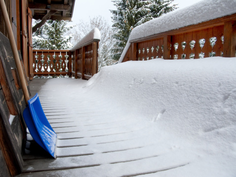 thick snow layer on wooden balcony of chalet in the morning after snowfall with shovel in the European Alps