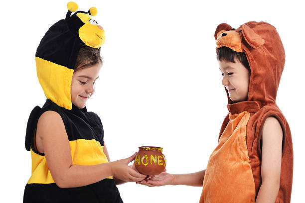 Bee and bear costume Girl dressed in a bee costume is giving a pot of honey to boy in a bear costume shot in studio on white background. bee costume stock pictures, royalty-free photos & images