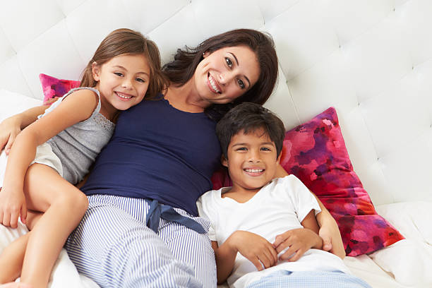 istock Smiling woman and two kids cuddling in a white bed 453564409