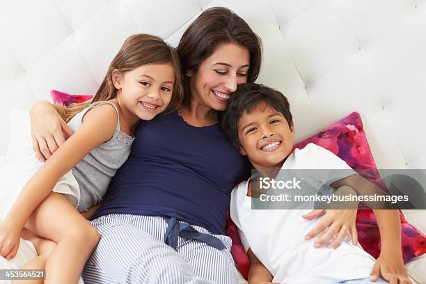 Mother And Children Relaxing In Bed Wearing Pajamas Stock Photo - Download Image Now