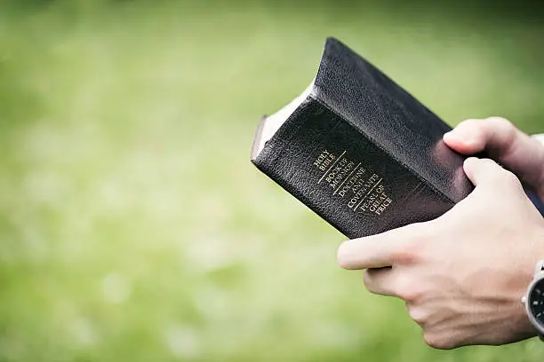 Hands of a young male missionary holding the "Quad" containing The Holy Bible, The Book of Mormon, Doctrine and Covenants and The Pearl of Great Price.