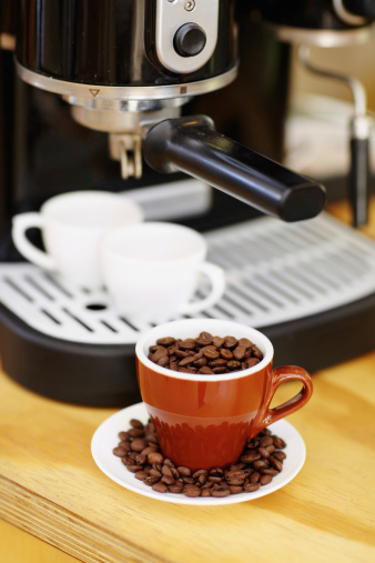 Shot of a mug full of coffee beans sitting in front of an expresso making machine