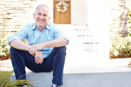 Senior man smiling while sitting outdoors in front of a house