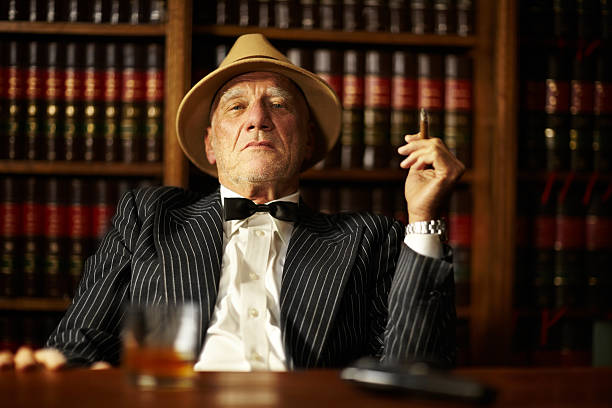 Crime is all about control Aged mob boss smoking a cigar and looking serious from behind his desk gangster photos stock pictures, royalty-free photos & images