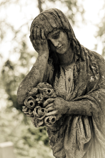 Lychakiv cemetery on Lviv, Ukraine. Lady stone statue from XIX century, she looks like crying, in sorrow. She´s hanging a flowers bouquet.