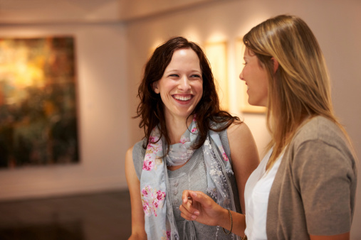 Two female friends share a laugh while attending an art exhibition