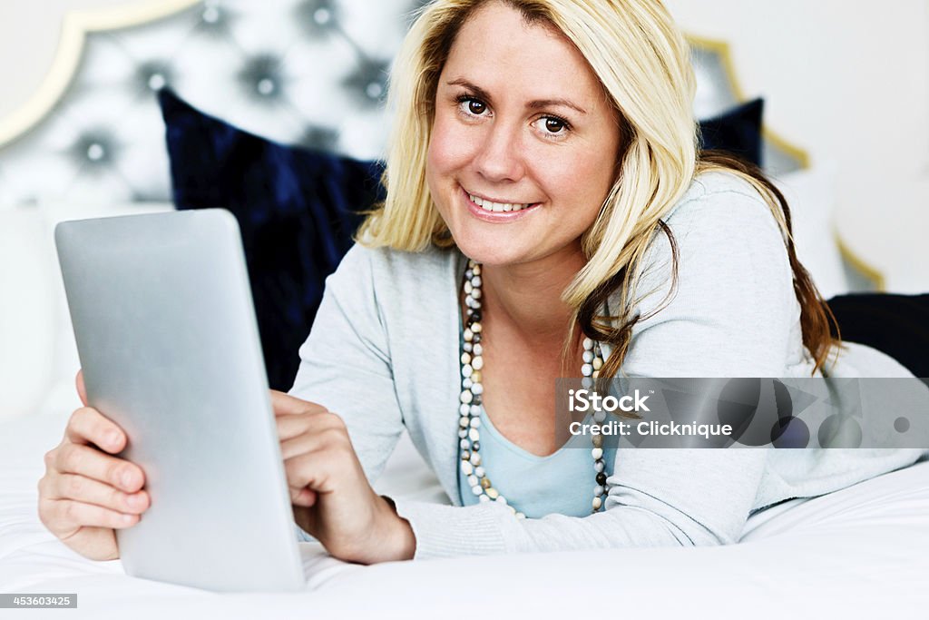 Linda rubia sonriente yacer en la cama usando tableta digital - Foto de stock de 20 a 29 años libre de derechos