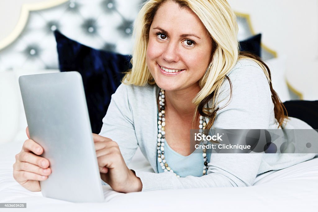 Linda loira sorridente Deitado na cama usando o tablet digital - Foto de stock de 20 Anos royalty-free