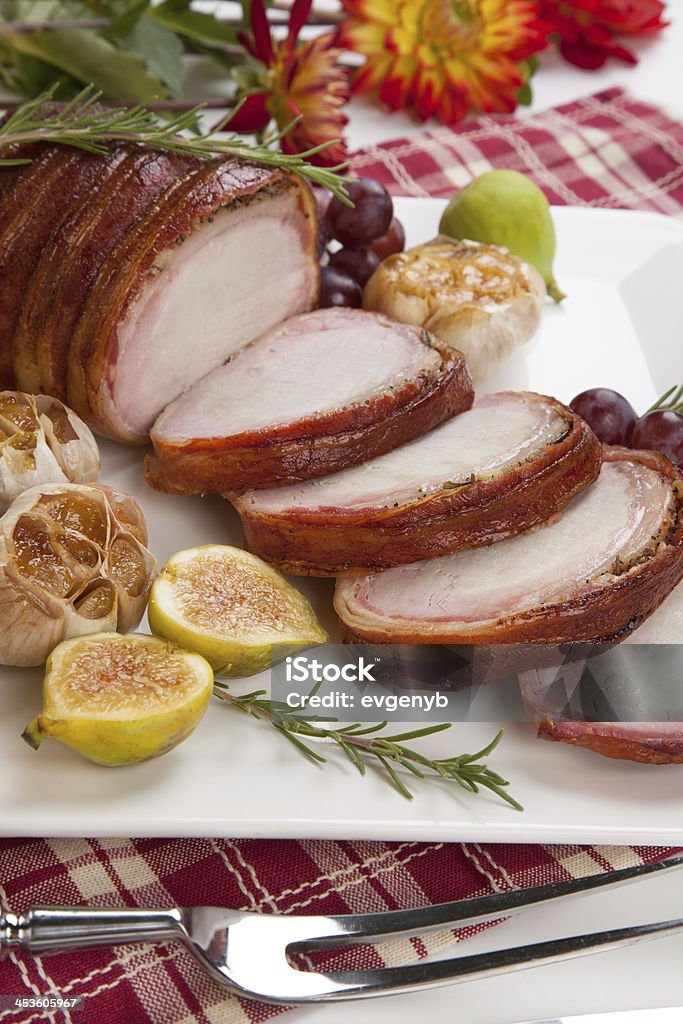 Bacon-wrapped Pork Loin with Fruits Closeup of delicious sliced roasted bacon - wrapped pork loin with roasted garlic, grapes, figs, and fresh rosemary. Bacon Stock Photo