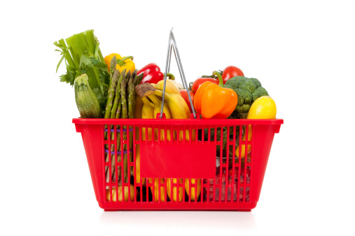 Red shopping basket with vegetables including peppers, asparagus, celery, tomatoes, squash and broccoli on a white background