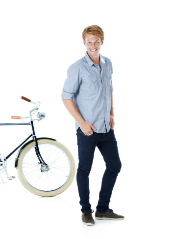 A handsome young red-headed man standing next to an old-fashioned bicycle with his hands in his pockets