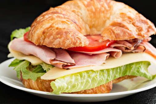 A close up shot of a ham and swiss cheese sandwich on a croissant.