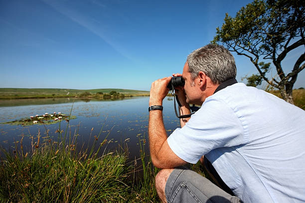 istock Mature caucasian man  through binoculars at lily pond 453647819
