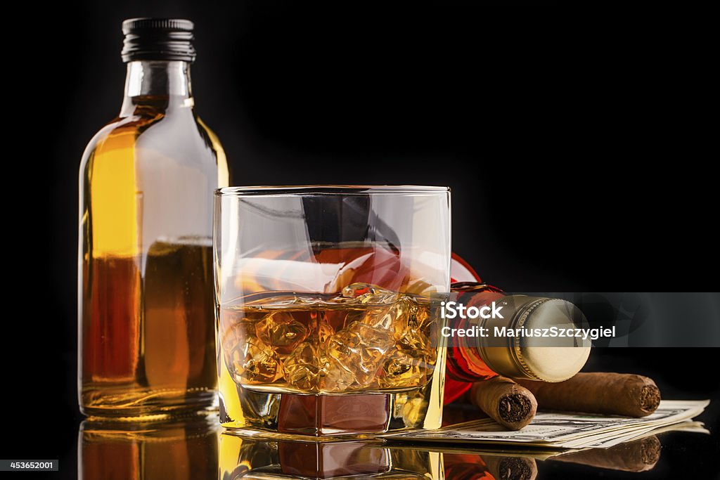 whisky glass whisky glass and bottles,  cigars and dollar money on reflecitve surface and black background Alcohol - Drink Stock Photo