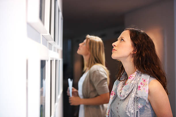 Closely examining the elements of a painting Two female friends viewing paintings while attending an exhibition exhibition stock pictures, royalty-free photos & images