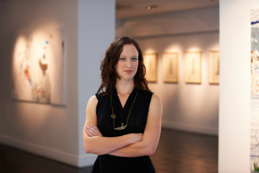 A portrait of a young woman standing in front of numerous paintings hanging on the walls of a gallery