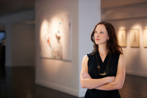 A young art dealer looking around at numerous fine art paintings hanging on the walls of a gallery