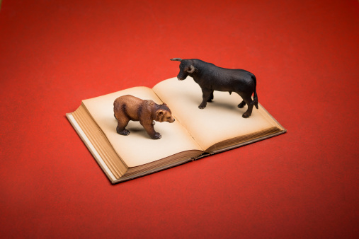 Old yellowed book with a miniature bull and bear. Shot on a red surface.