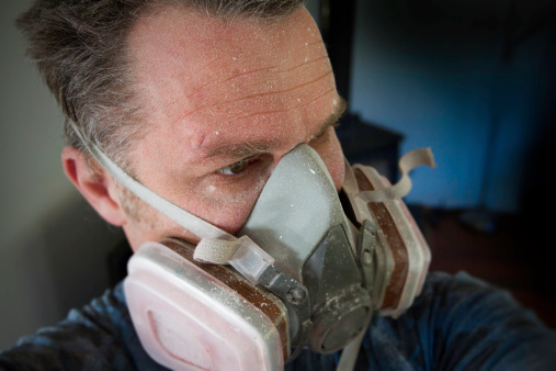 A man wears a protective respirator while plastering plaster board in a house. The dust from sanding is  bad for your health if breathed.