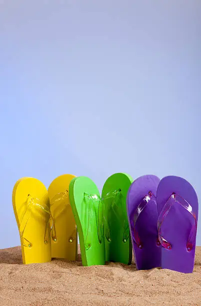 Four pairs of colorful flip-flop sandals on a beach background, studio shot