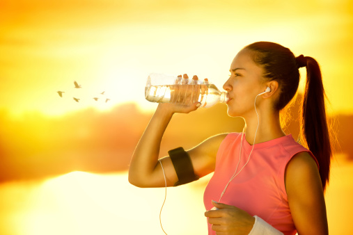 Sporty woman drinking water outdoor on sunny day