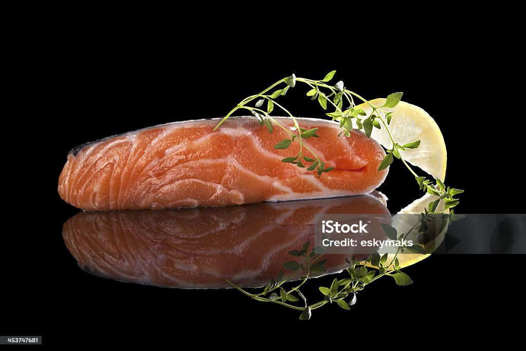 Luxurious salmon steak. Fresh raw salmon steak with lemon and thyme isolated on black background with reflection. Luxurious seafood eating. Black Background Stock Photo