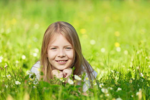 Cute smiling little girl hiding in the grass on the summer field